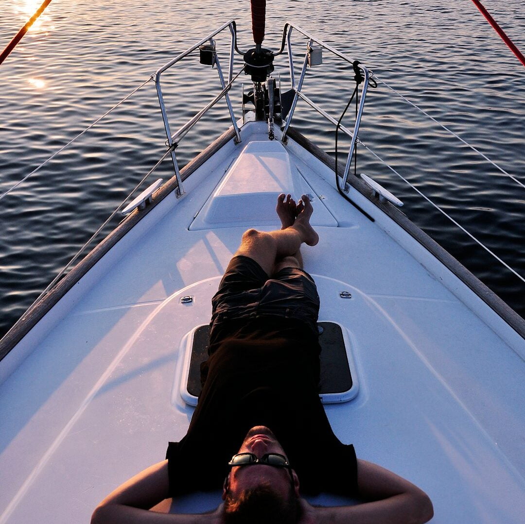 Person relaxing on the bow of a boat, arranged through boat rental software, during sunset. | kleesto